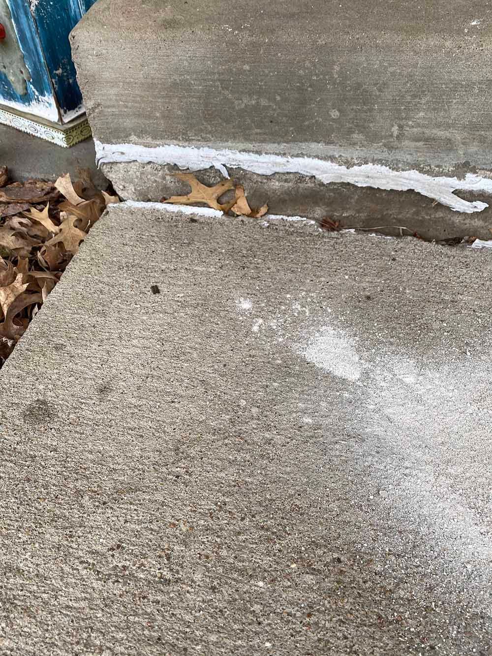 A person is painting a concrete sidewalk with a brush.