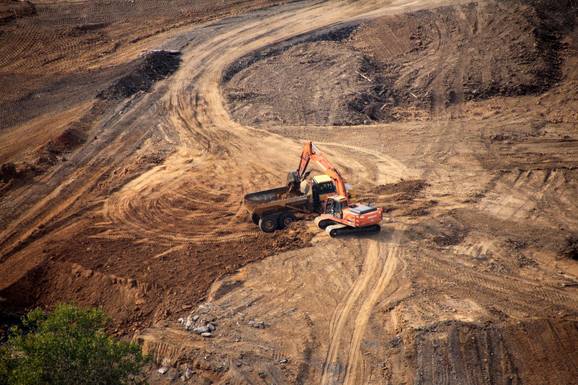 Excavator and dump truck working on a barren dirt construction site with winding tire tracks