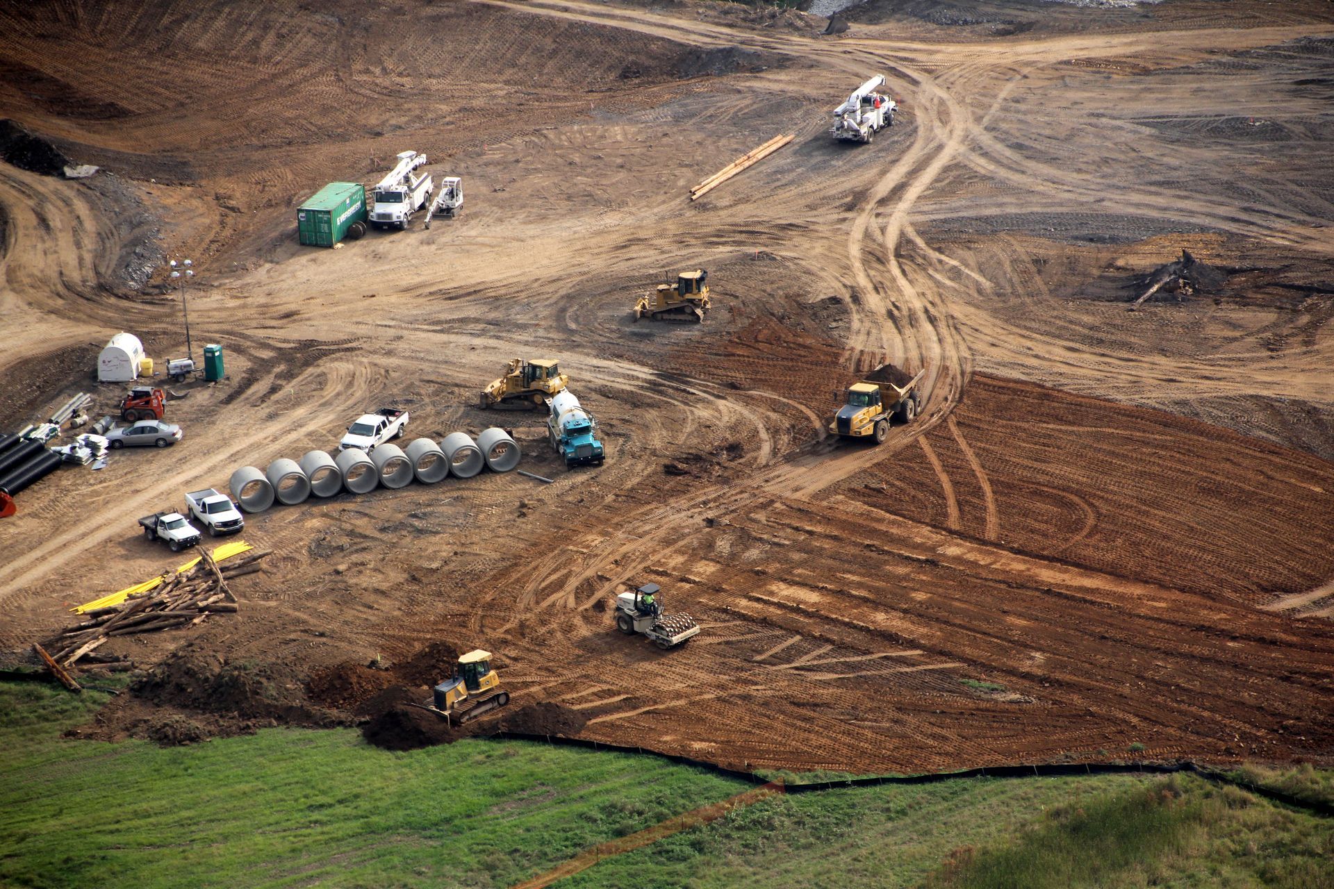 Aerial view of heavy machinery grading a large brown dirt construction site with trucks and tracks.