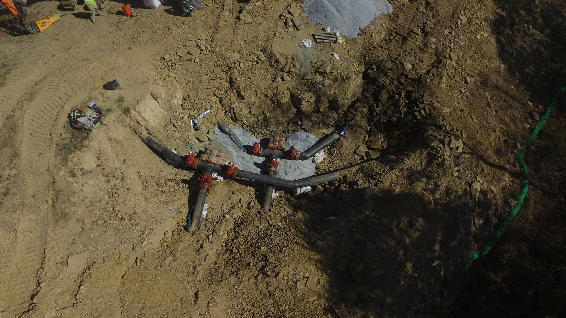 Person using a black-and-red drone controller on dirt ground, with green cable nearby