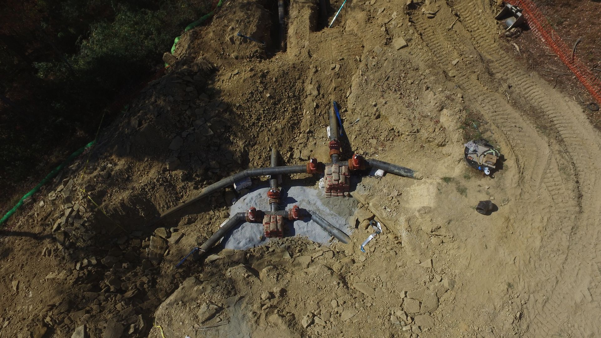 Three workers on a sandy construction site installing or repairing a buried pipe.