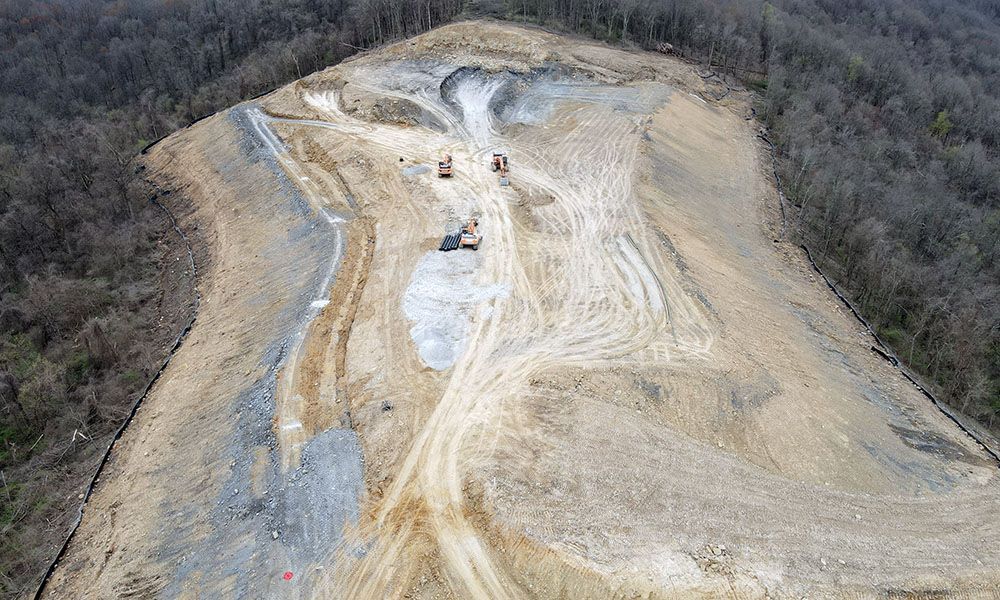 Aerial view of a large, dusty quarry cut into a forested hillside.