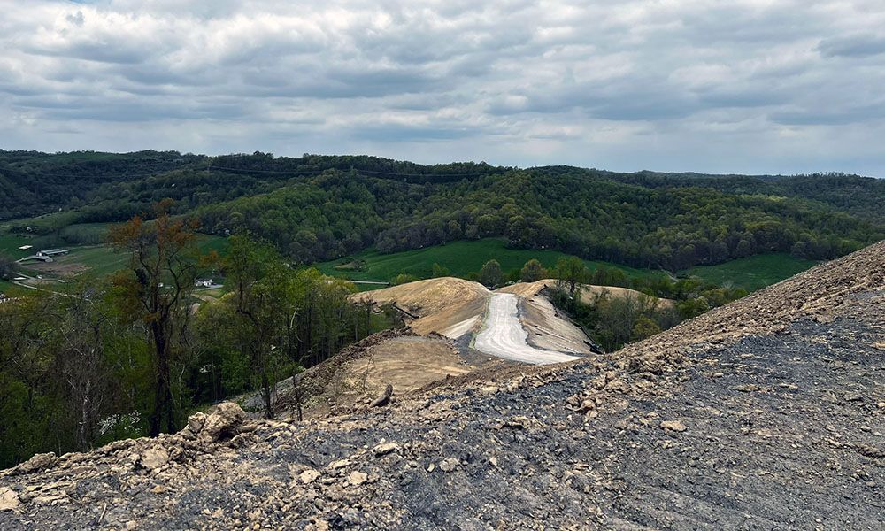 Winding dirt road through rocky terrain and green forested hills under a cloudy sky