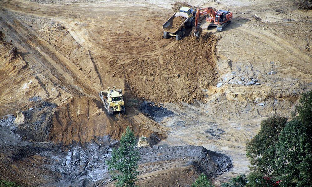 Bulldozers and dump trucks working on a muddy construction site with dirt piles and tire tracks