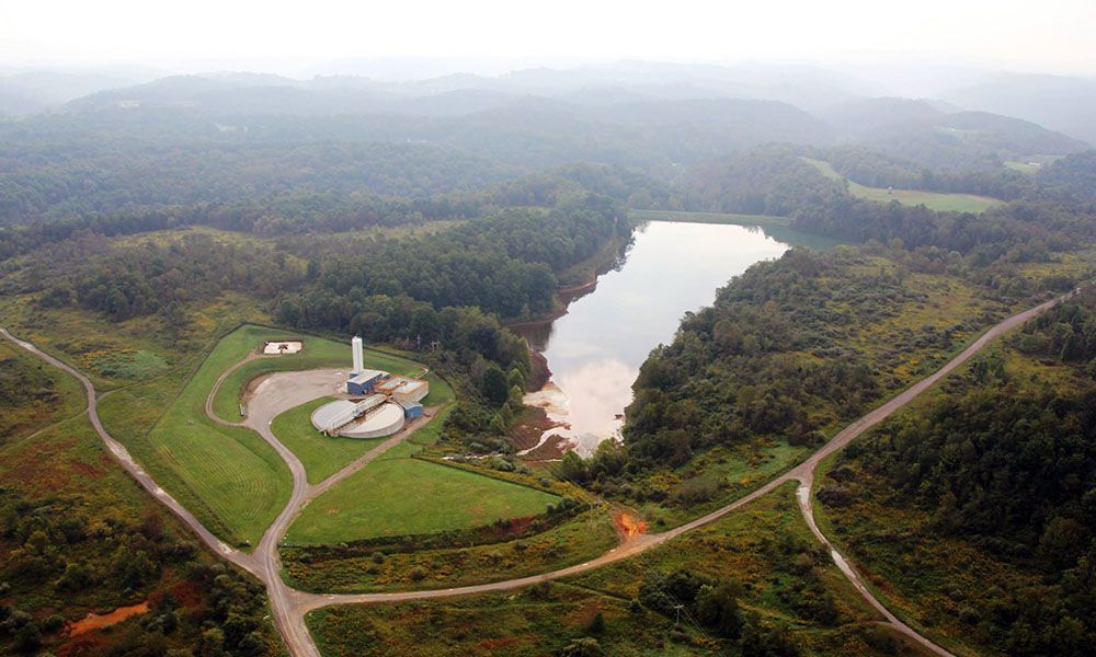 Aerial view of a forested landscape with a lake, roads, and a small industrial facility with a white tower
