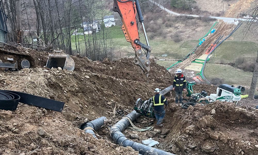 Workers in a muddy landslide area near a large pipe and excavator on a hillside site