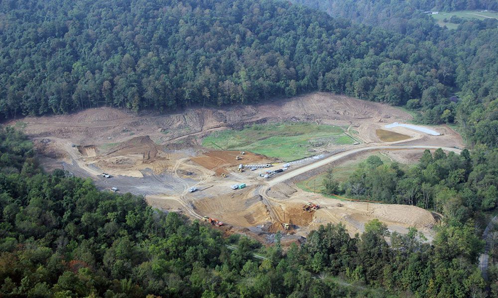 Open-pit mine clearing surrounded by dense green forest, with exposed earth and dirt roads