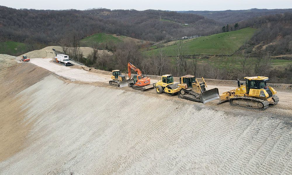 Road construction with several yellow excavators and a truck working on a hillside gravel embankment.