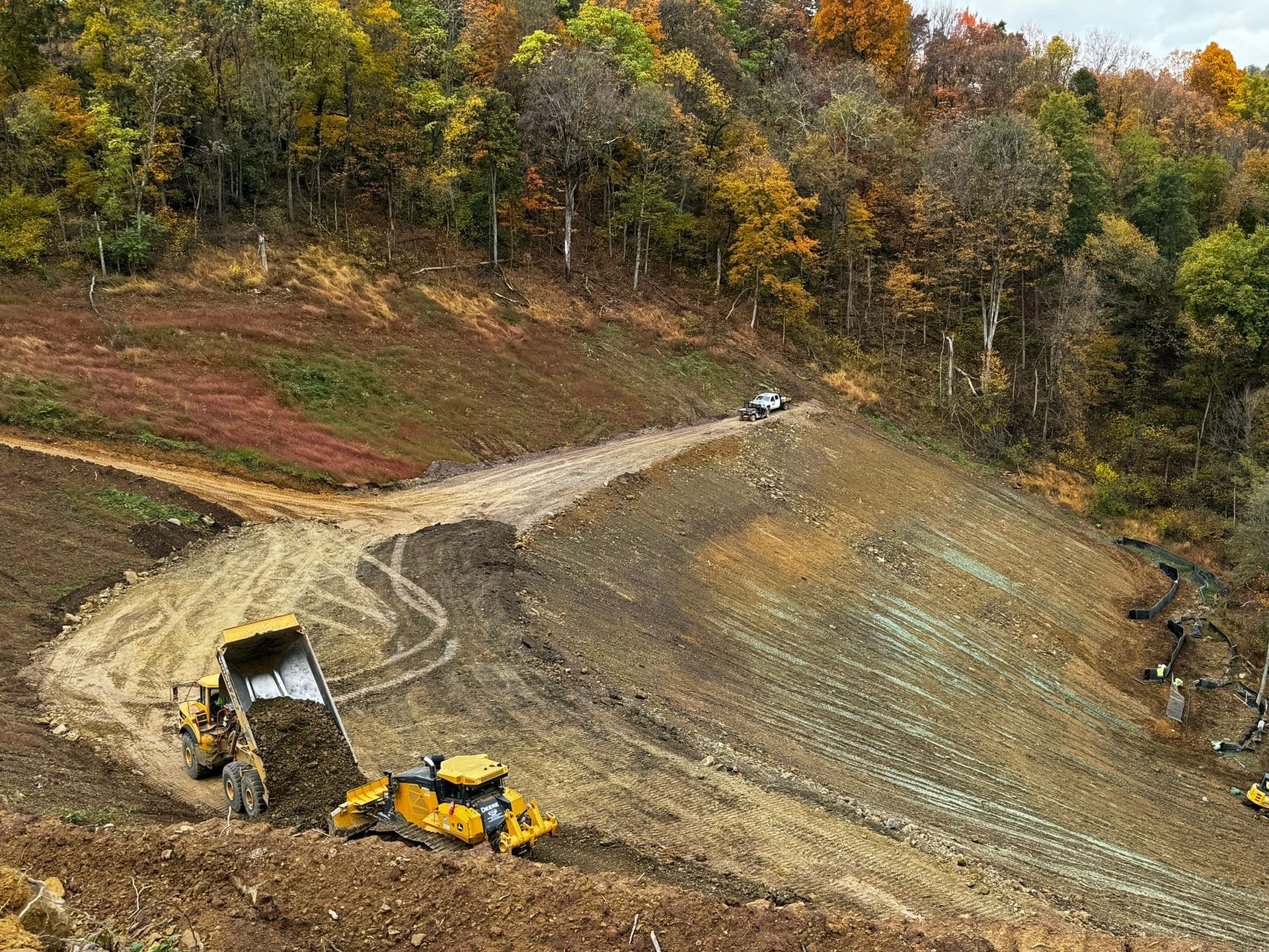Bulldozer grading a dirt road on a steep hillside with autumn trees in the background