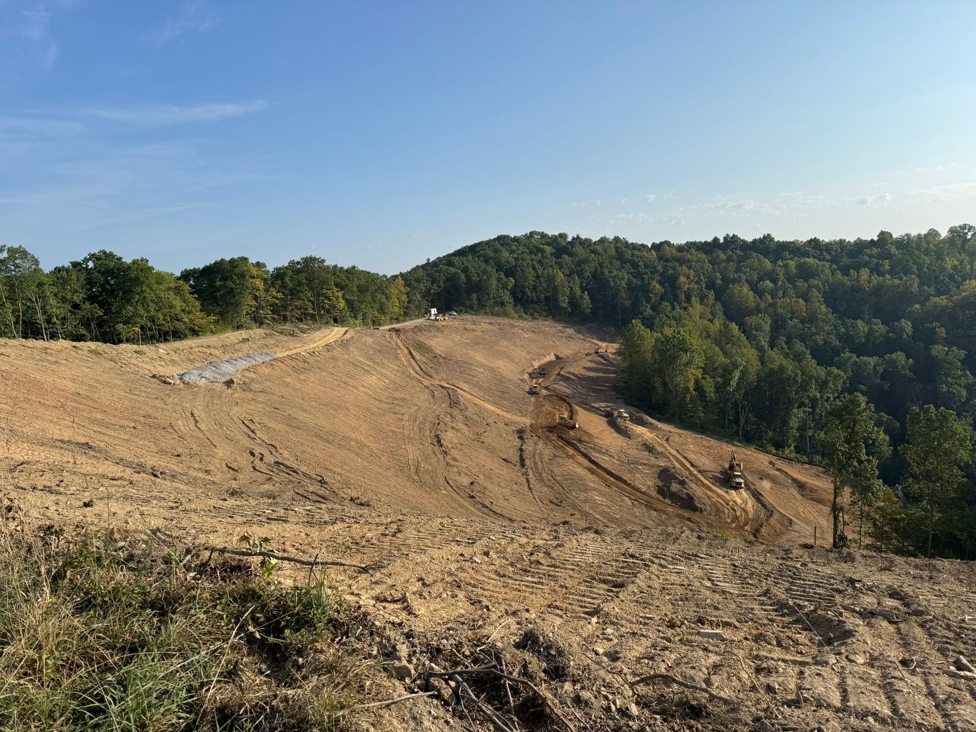 Cleared hillside with exposed soil and trees under a clear blue sky