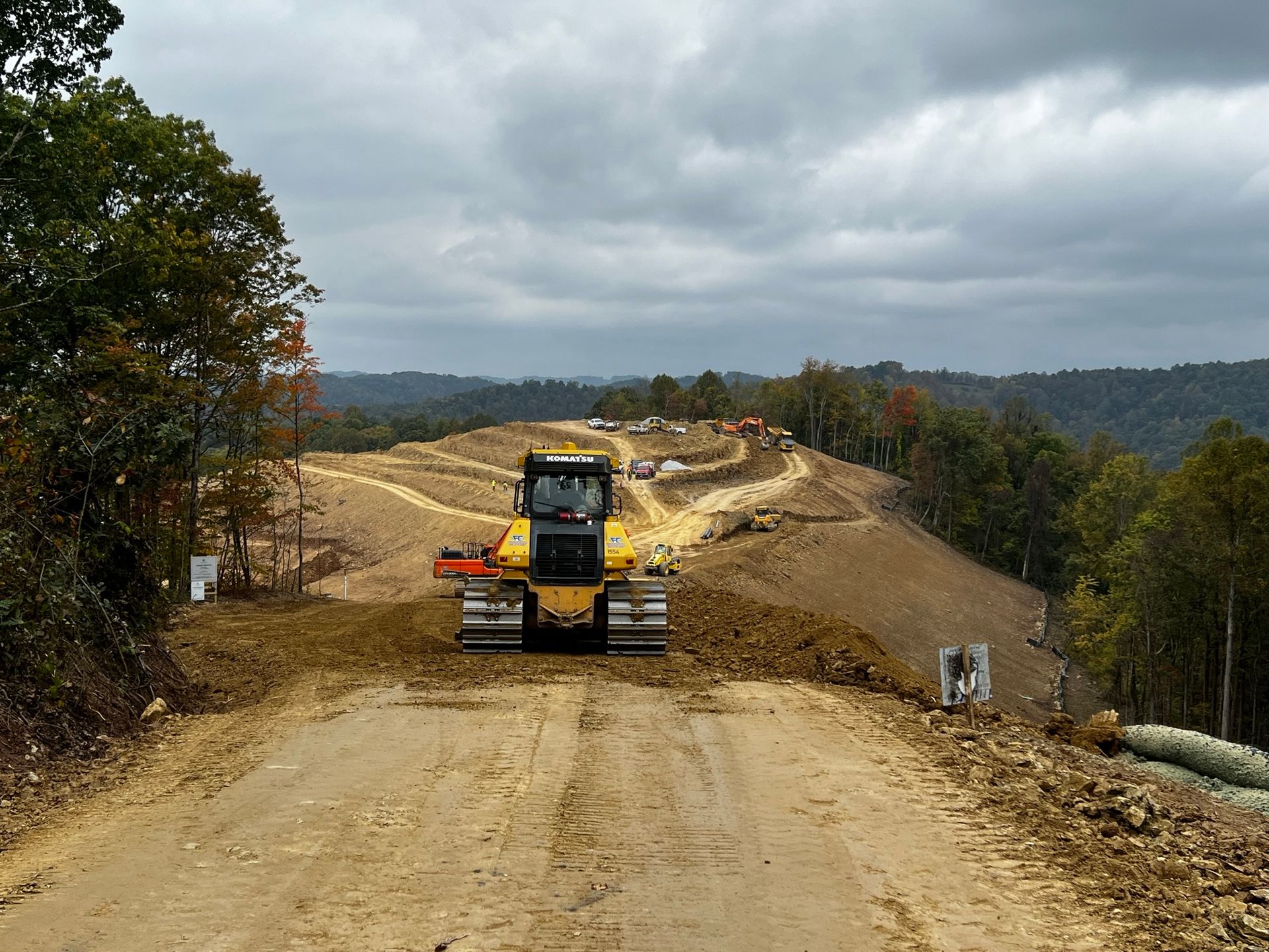 Construction vehicle on a dirt road under cloudy skies, grading a rough hillside road