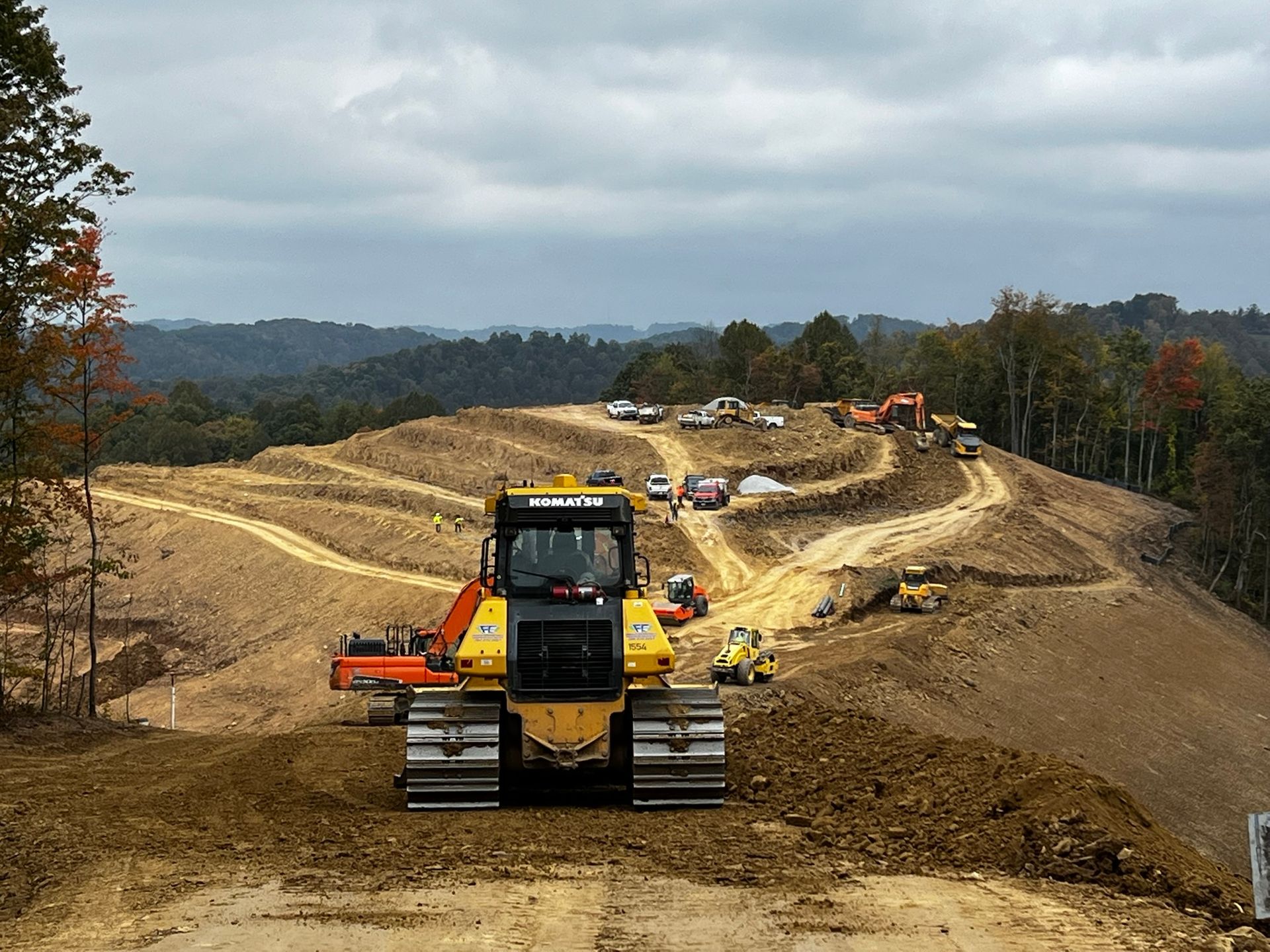 Yellow bulldozer on a dirt road at a hillside construction site under cloudy skies