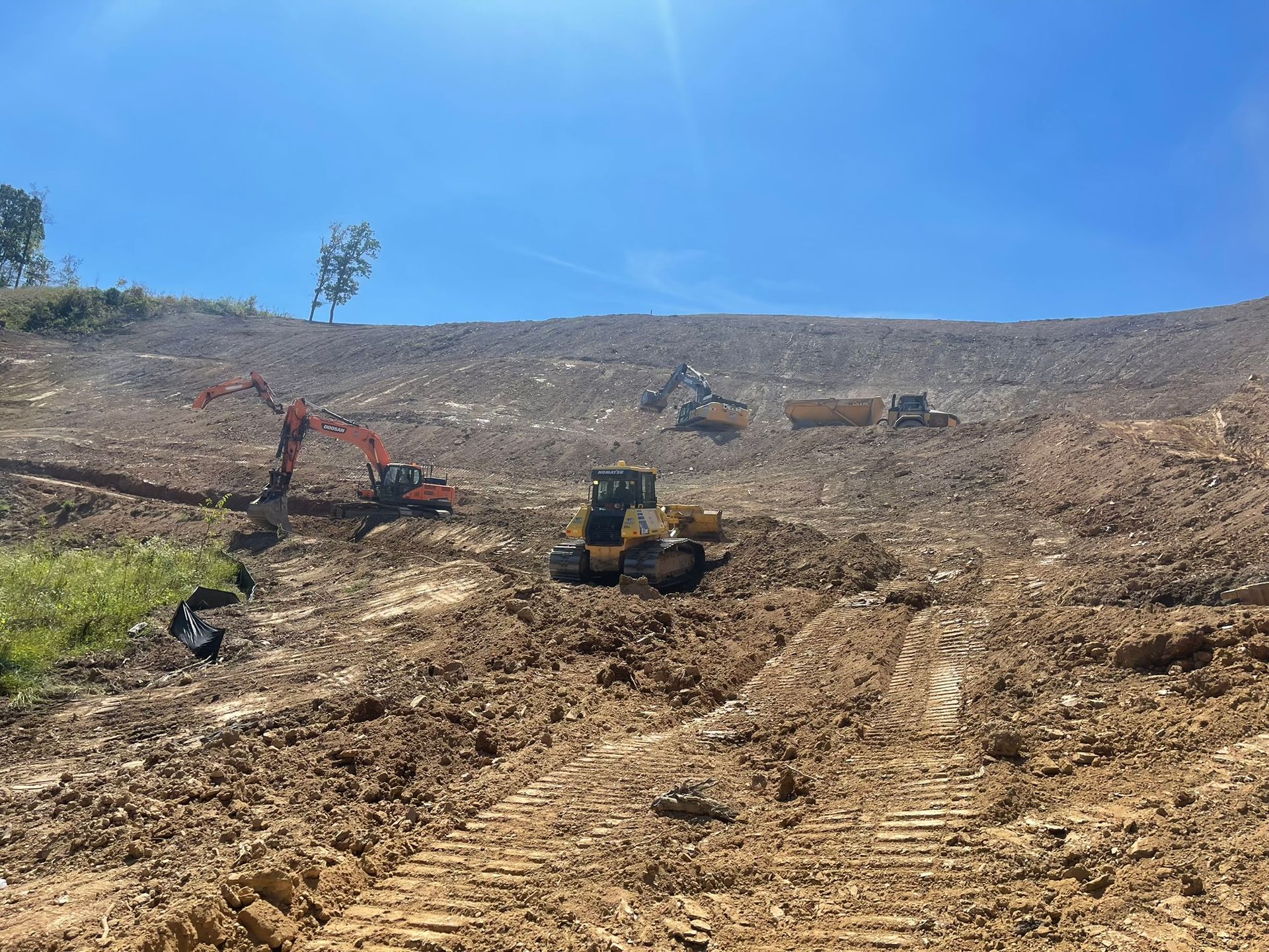 Heavy machinery clearing a barren hillside under a bright blue sky