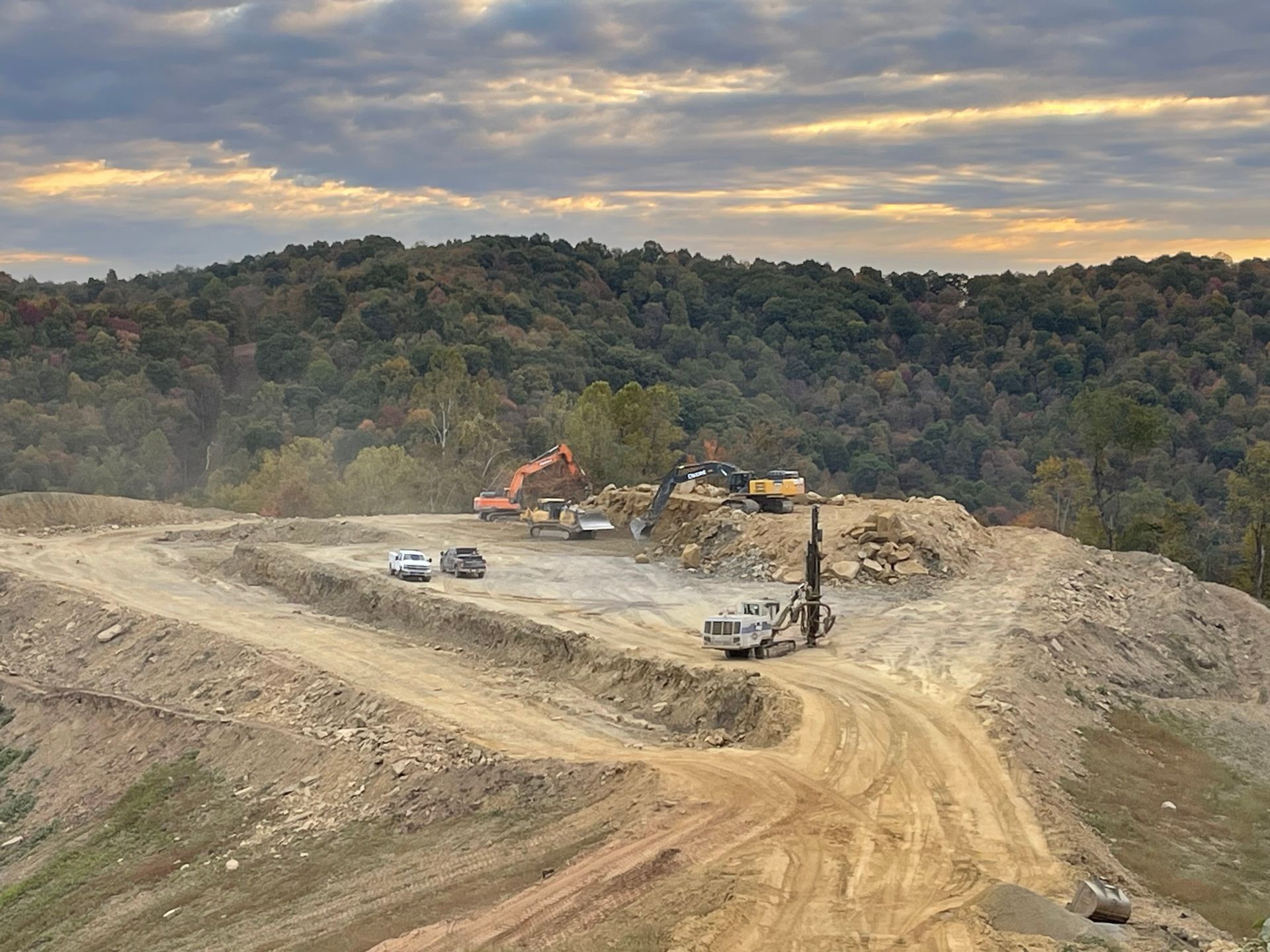 Mining site with excavators and trucks on a dusty hillside under a cloudy sky
