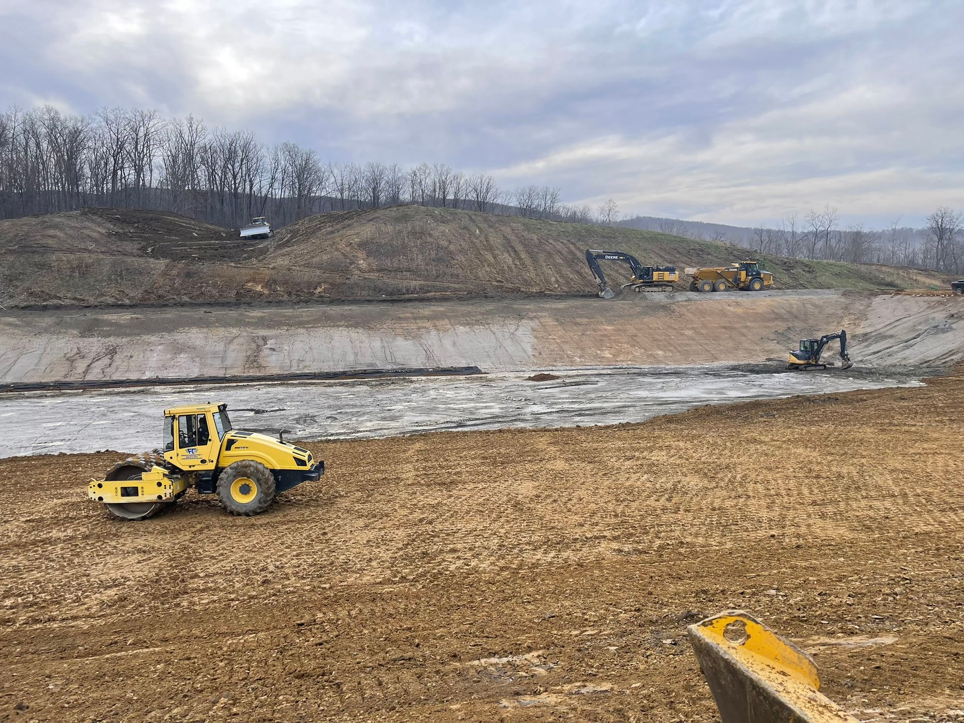 Yellow construction loader on muddy excavation site with dirt piles and overcast sky
