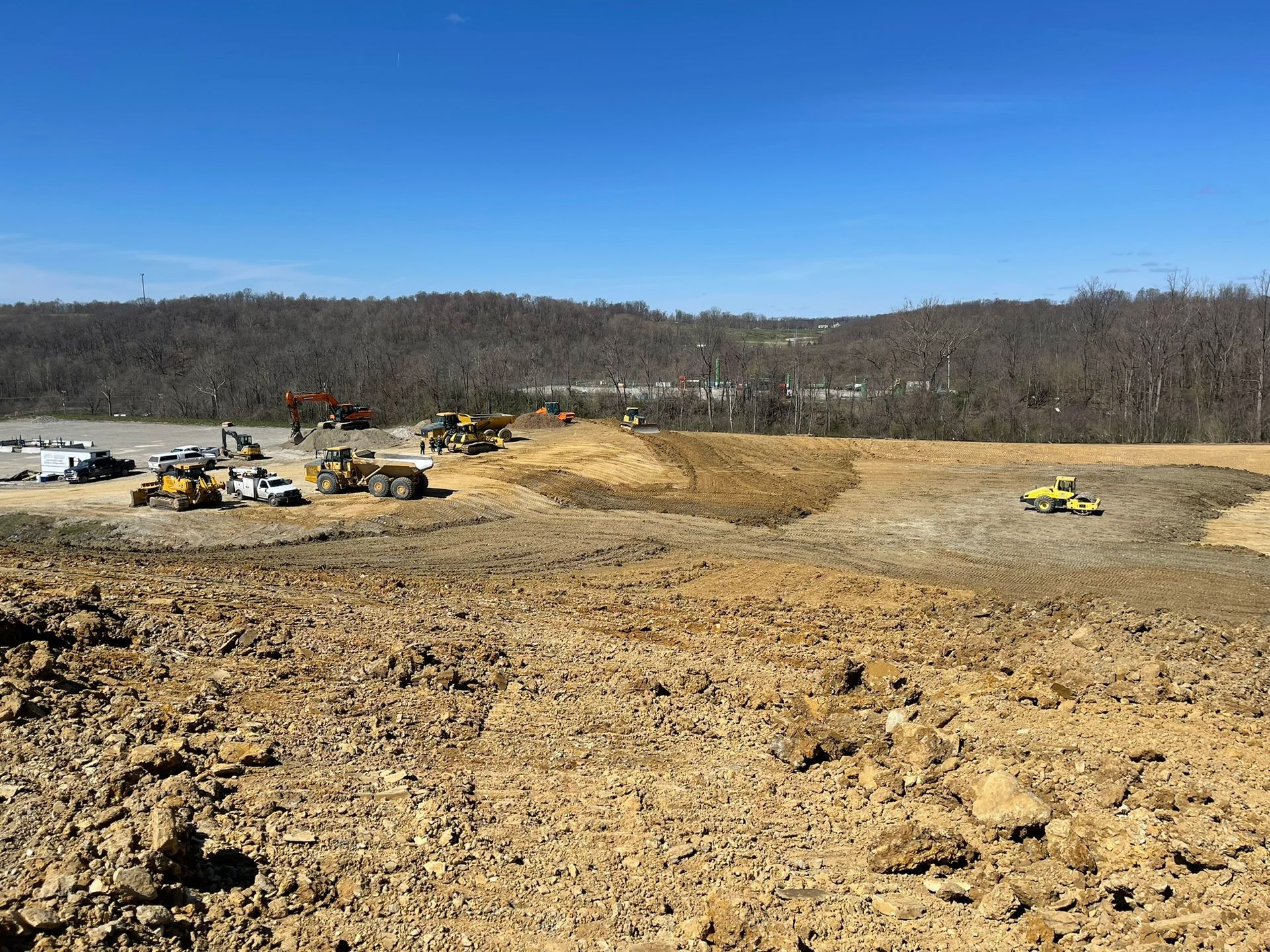 Construction site with excavators and trucks on a cleared dirt field under a blue sky