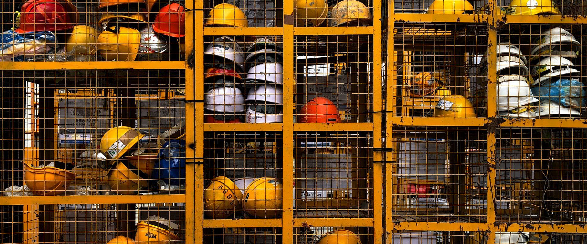 Rows of colorful hard hats and helmets stored behind wire mesh in an industrial rack