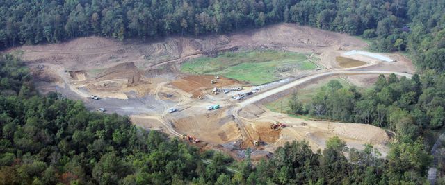Aerial view of a large open-pit mine surrounded by dense green forest.