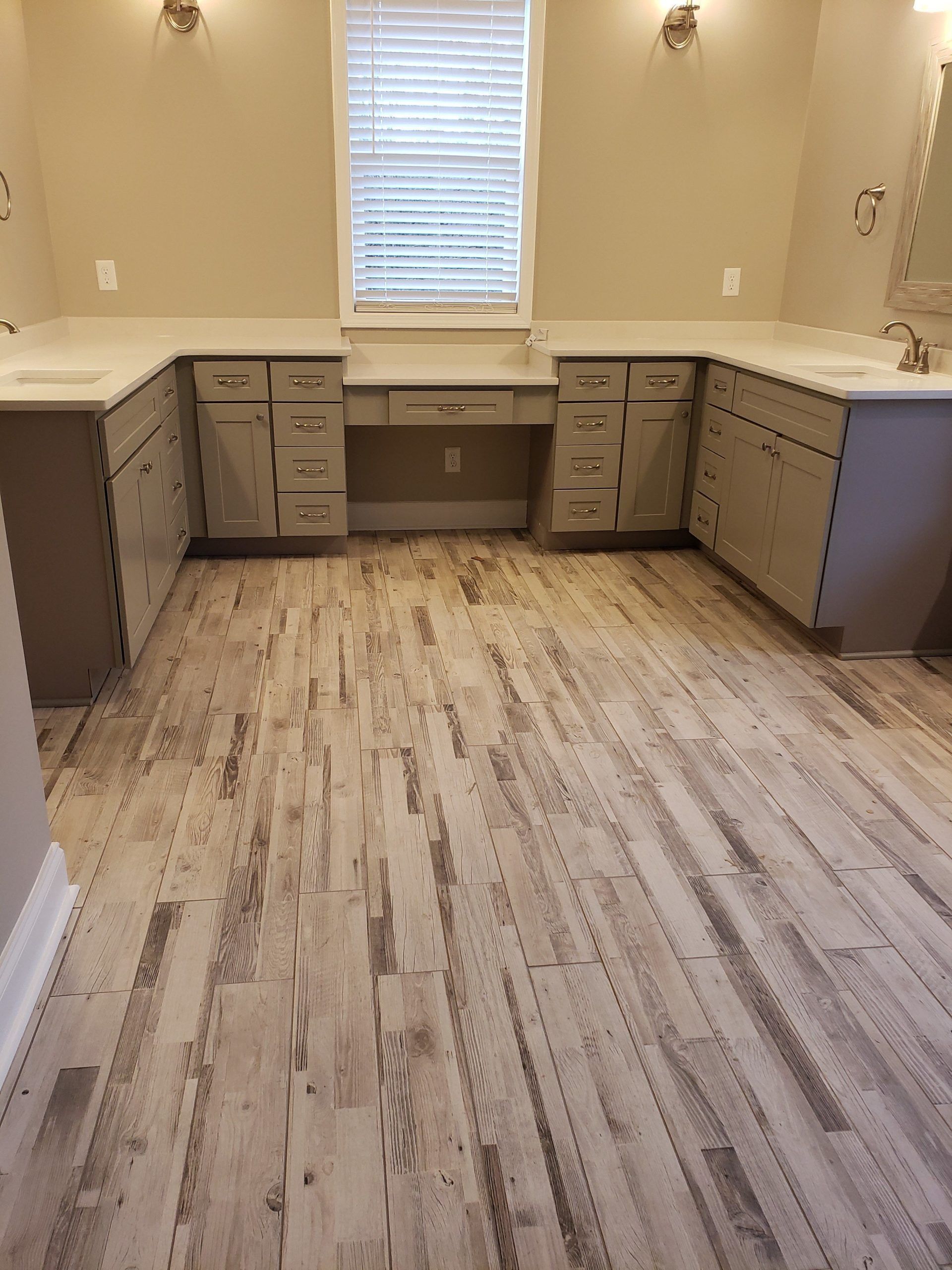 A bathroom with light gray cabinetry, double sinks, a central vanity desk, and wood-patterned flooring.