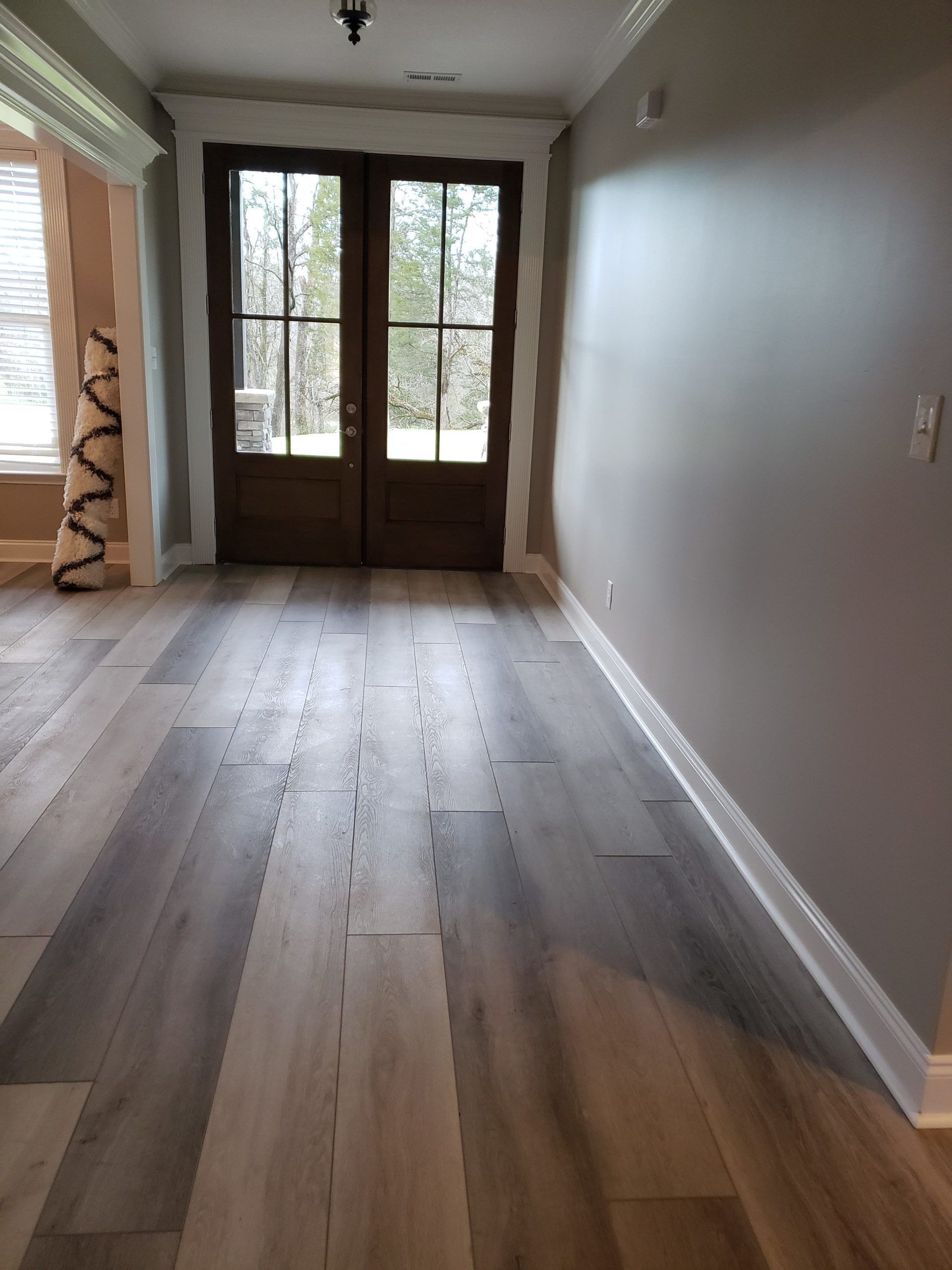 A view of a home entryway featuring light-to-dark gray wood-look flooring leading to a pair of dark wooden double doors.