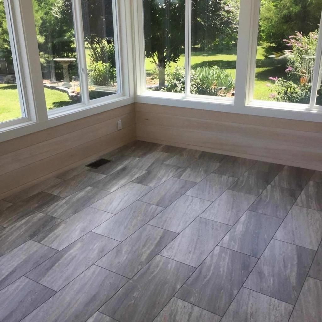 A bright sunroom with light-colored horizontal wall paneling, large windows, and grey wood-look tiled flooring.