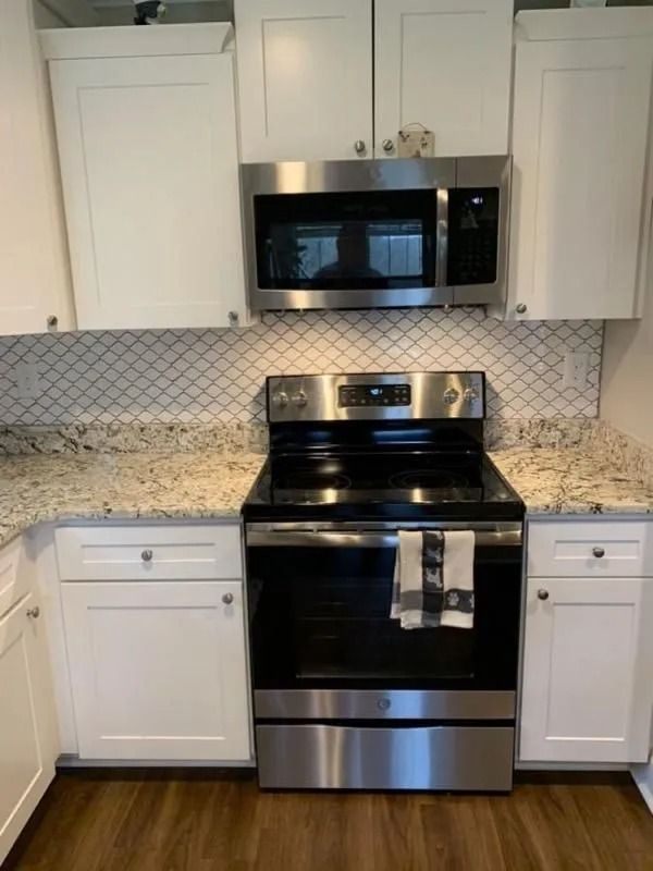 White kitchen cabinets, stainless steel oven and microwave, granite countertops, and decorative tile backsplash.