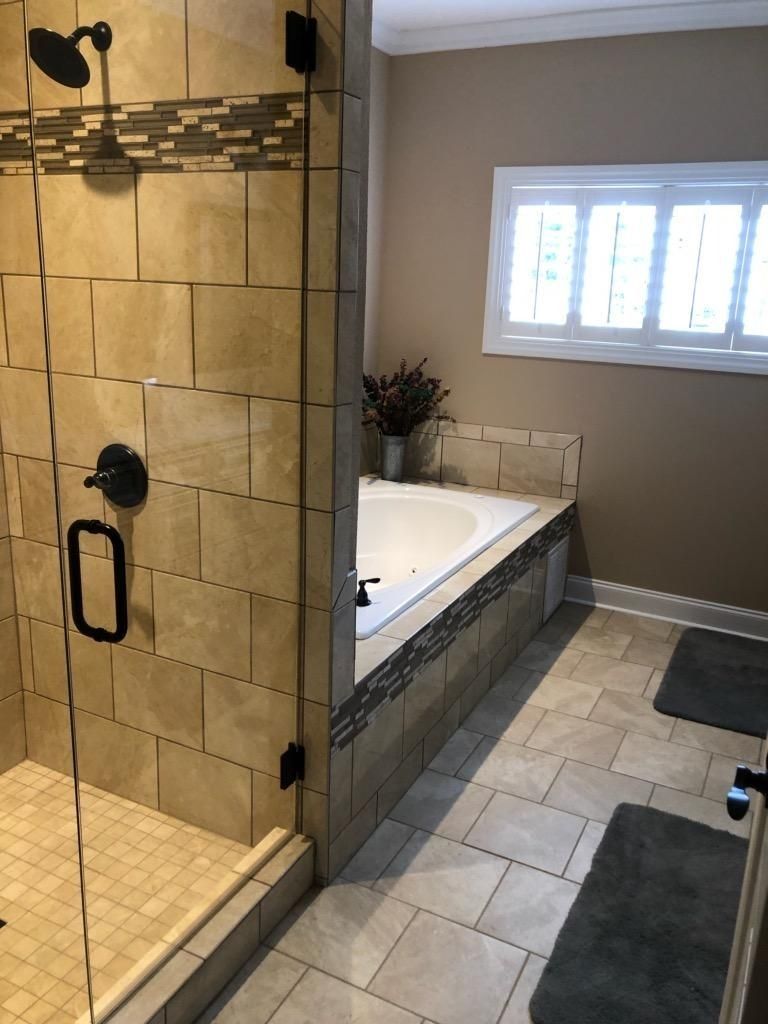 A bathroom with a tiled walk-in shower and a built-in bathtub under a window, featuring neutral-toned stone tiles.
