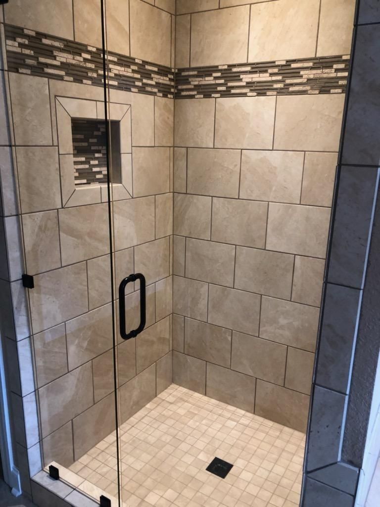 A shower enclosure with beige rectangular tiles, a horizontal mosaic accent strip, a small recessed niche, and glass door.