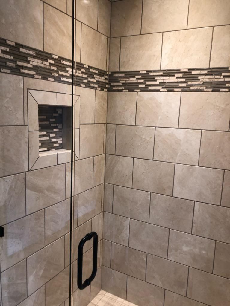 Shower enclosure with neutral rectangular wall tiles, a glass door, and a decorative horizontal mosaic tile accent strip.