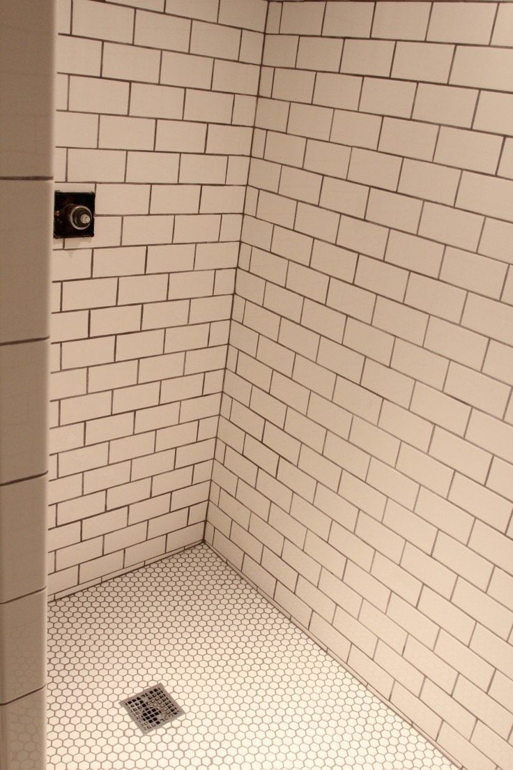A shower stall featuring white subway tile walls, a circular penny-tile floor, and a square central drain.