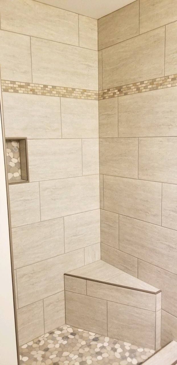 A tiled shower interior featuring neutral-toned rectangular wall tiles, a corner bench, a mosaic strip, and a recessed nook.