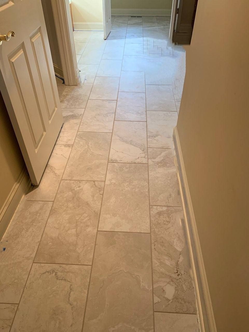 A hallway with light-colored, textured stone floor tiles extending from the foreground toward an open doorway.