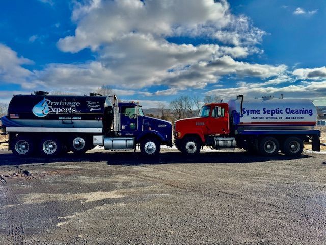 Two septic tank trucks parked side-by-side on a sunny day. One is blue, the other red, both with company logos.
