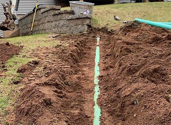 Dug trench with green pipe laid in it, likely for drainage or utility installation.