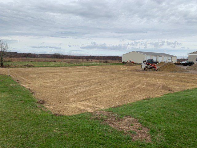 Dirt field being prepared for construction, with a small bulldozer and piles of dirt. Cloudy sky.