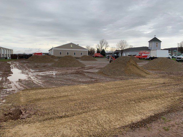 Construction site with piles of gravel and muddy ground under an overcast sky.