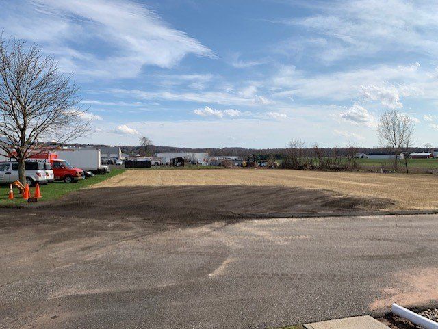 Cleared land, brown dirt, blue sky, white clouds, buildings in the distance.