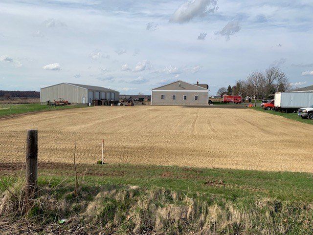 Cleared field, farm buildings, cloudy sky, dirt road.