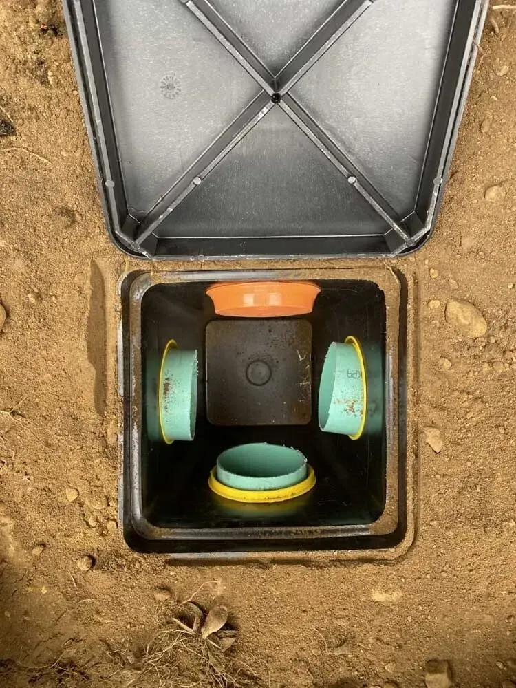 Open irrigation valve box with colored pipe fittings.