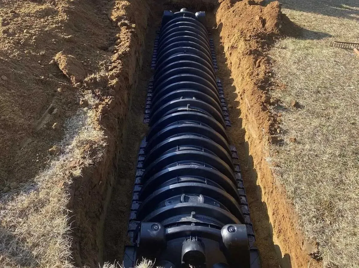 Black corrugated pipe installed in a brown trench outdoors on a grassy area.