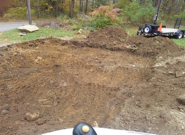 A dirt excavation site with tire tracks, a trailer, and a pile of soil in a grassy, outdoor setting.