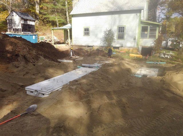 Construction site with exposed concrete septic tank components and soil near a house.