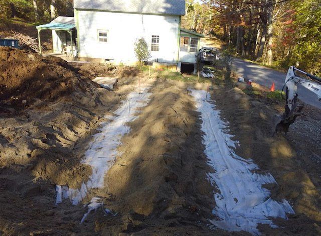 Construction site with house in background, soil, white fabric, and excavator.