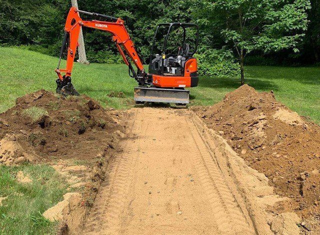 Orange mini excavator digging a trench in a grassy yard, with two piles of dirt on either side.
