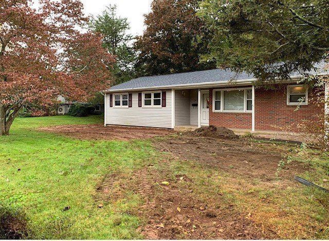 Ranch-style house with brick and siding, brown shutters, and overcast sky. Bare dirt and grass in yard.