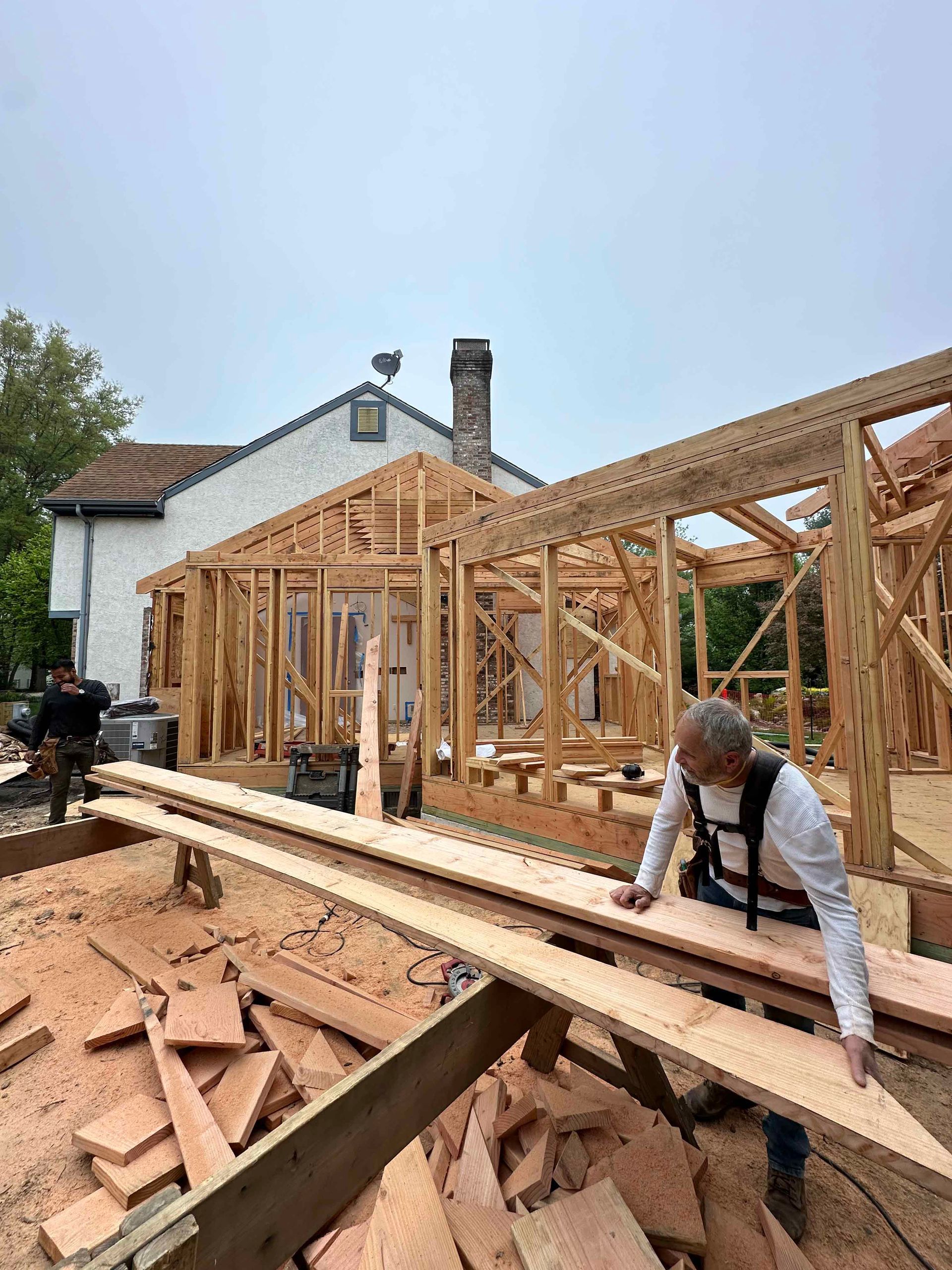 A man is holding a piece of wood in front of a house under construction.