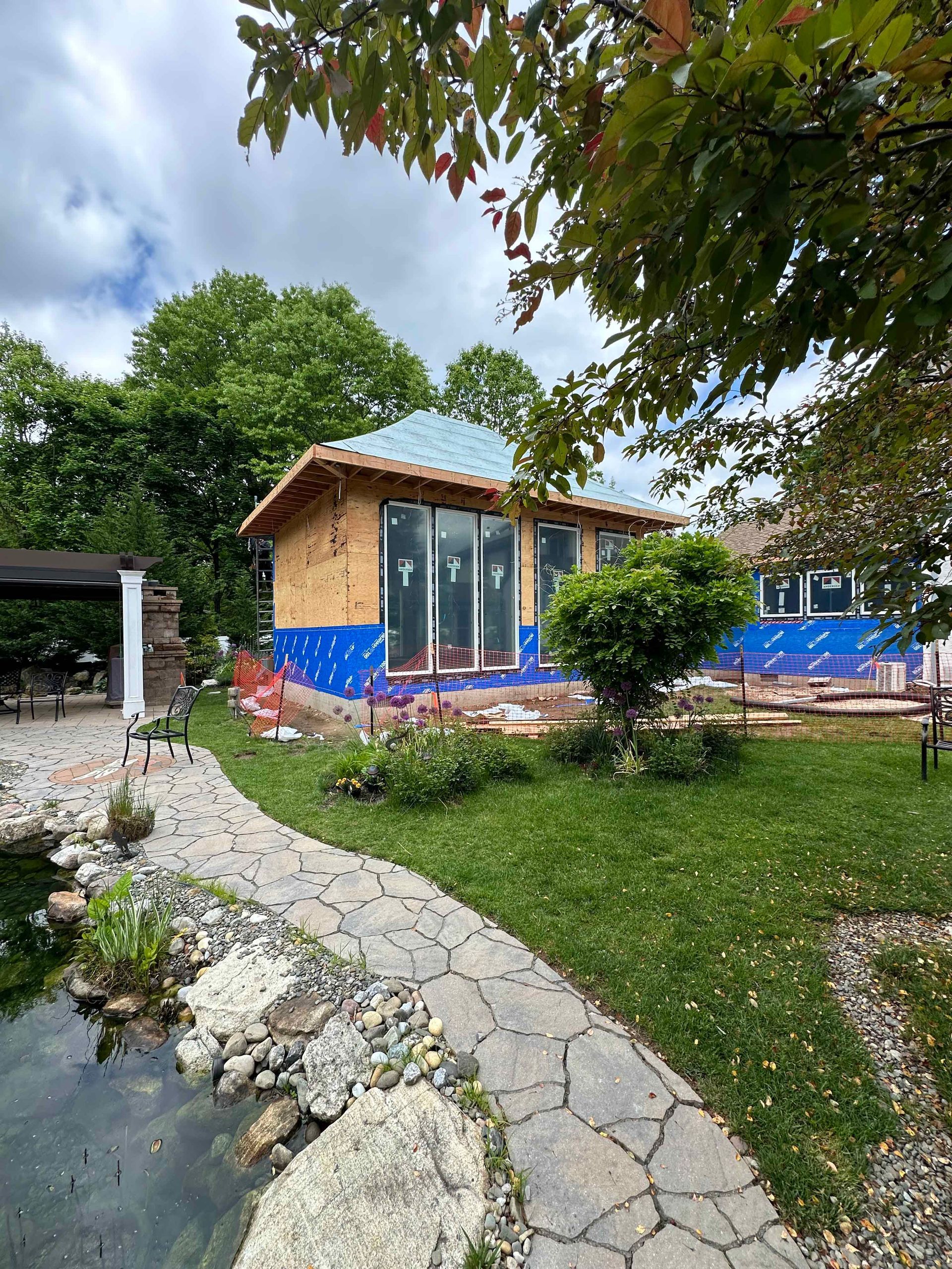 A house is being built in a backyard next to a pond.