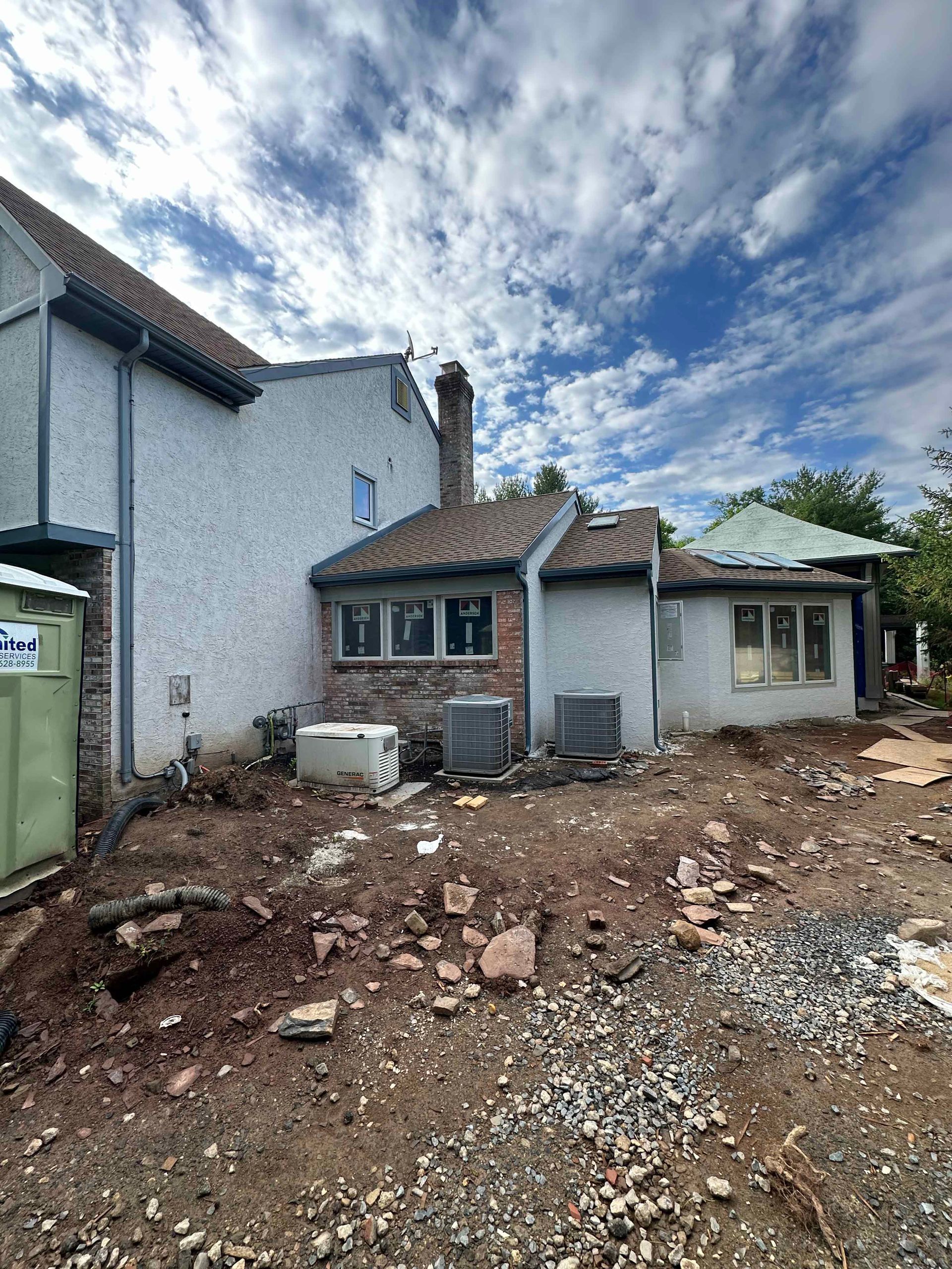 A white house with a brick roof is sitting on top of a dirt field.