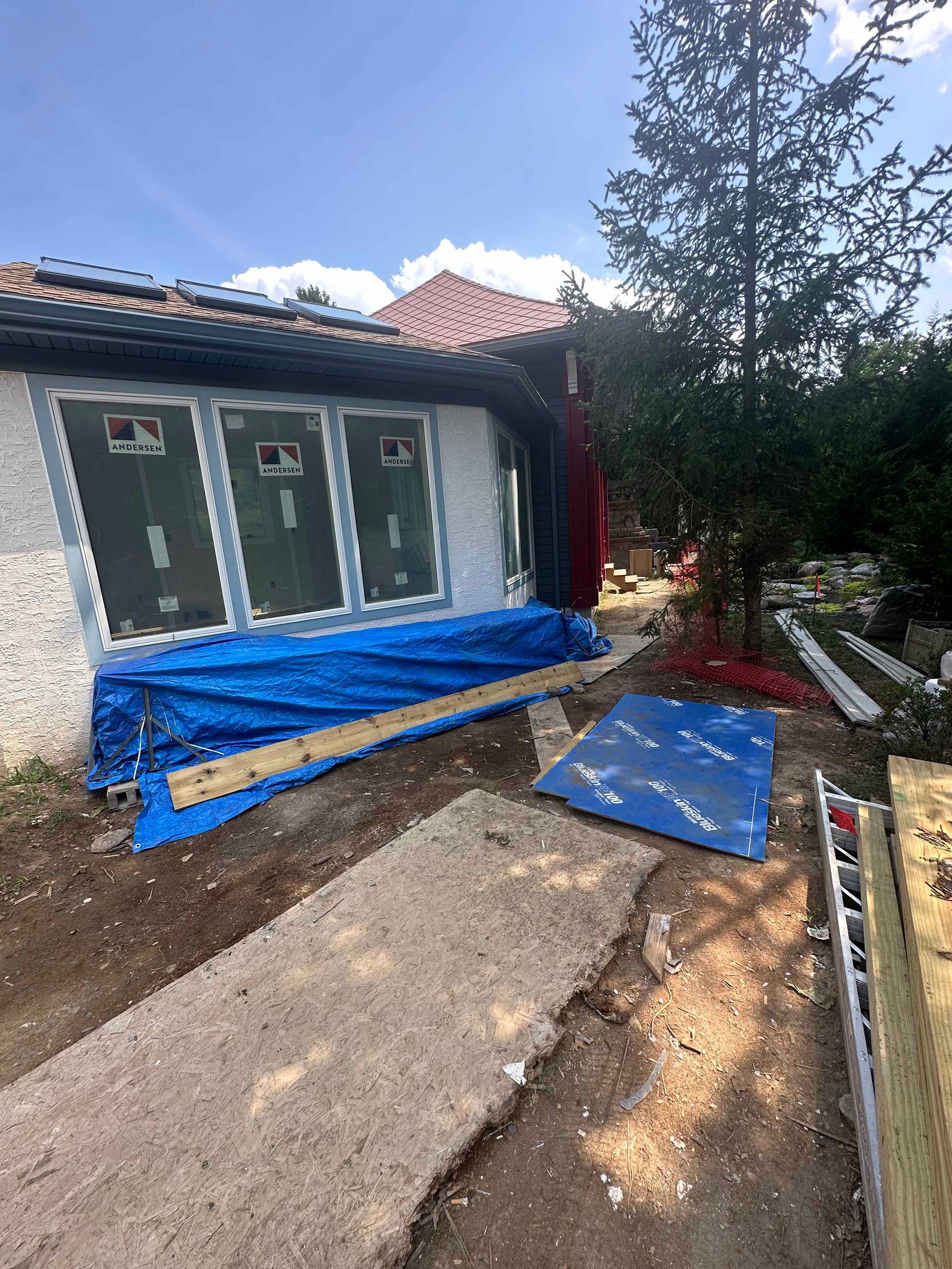 A house is being built with a blue tarp on the side of it.