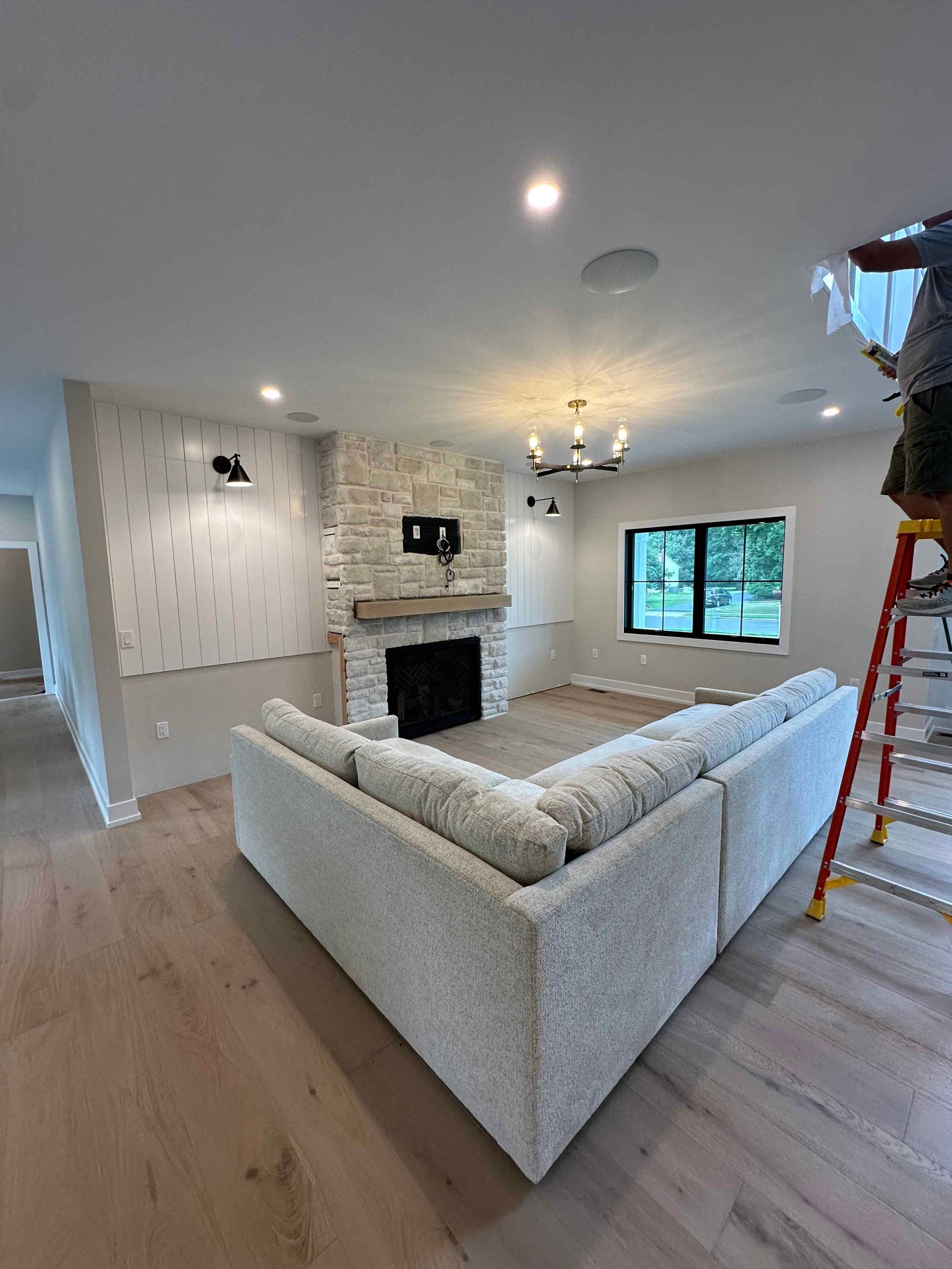 A man is standing on a ladder in a living room with a couch and fireplace.